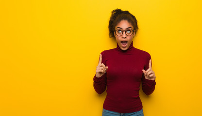 Wall Mural - Young black african american girl with blue eyes surprised pointing up to show something