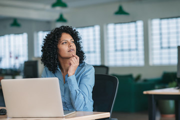 young businesswoman thinking while using a laptop at work