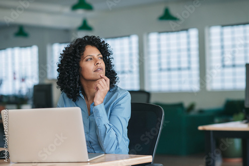Fotomural Young businesswoman thinking while using a laptop at work