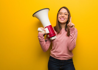 Wall Mural - Young cute woman holding a megaphone showing number one