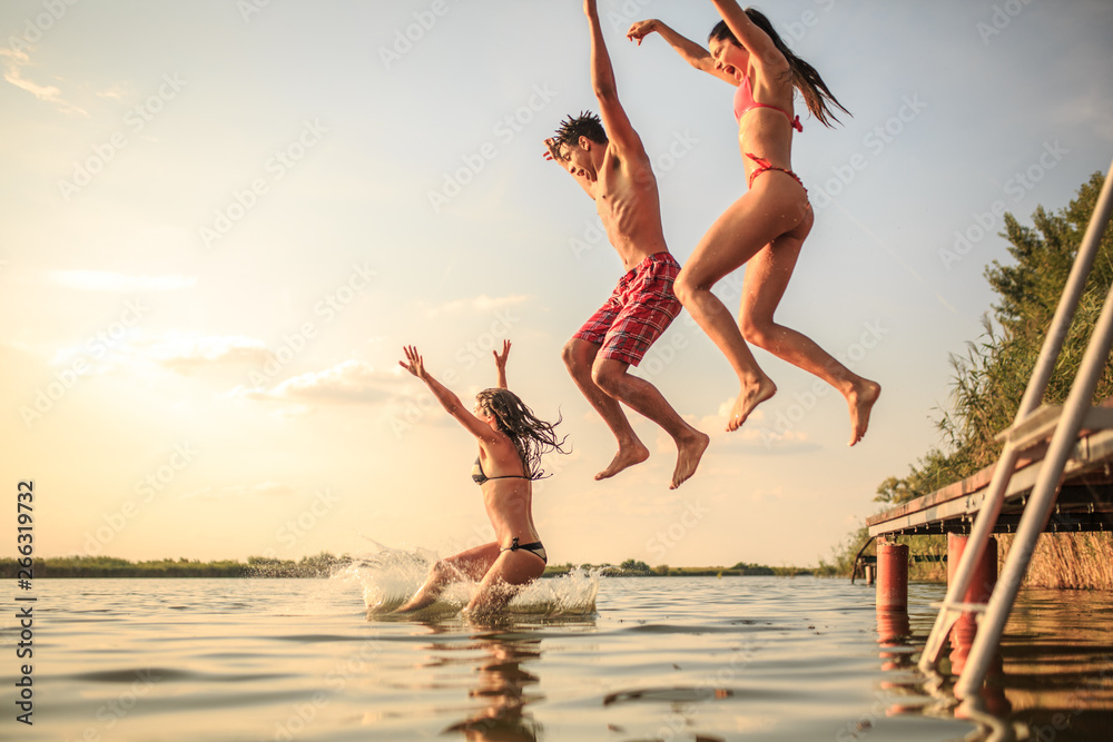 Group of friends jumping into the lake from wooden pier.Having fun on summer day. - obrazy, fototapety, plakaty 