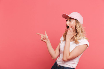 Canvas Print - Portrait of trendy blond woman 20s wearing casual t-shirt and cap pointing fingers aside at copyspace