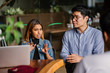 © Danon - Two young Asian entrepreneurs dressed professionally are sitting at a cafeteria table and having an animated discussion during the day.