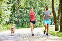 Happy Couple Running With Dog In Park