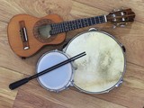 Three Brazilian musical instruments: cavaquinho, pandeiro (tambourine) and tamborim with drumstick on a wooden surface. The instruments are widely used to accompany samba music.