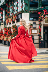 Wall Mural - christmas portrait of beautiful woman with blond hair, wearing long red dress, walking down the stre