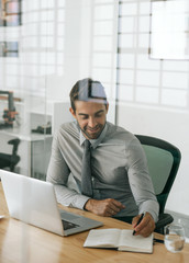 Smiling businessman sitting at work writing ideas in a notebook