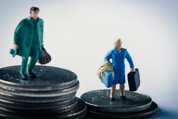 miniature woman and man on piles of dollar coins