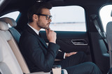 Fototapeta  - Thinking about solution. Thoughtful young man in full suit keeping hand on chin while sitting in the car