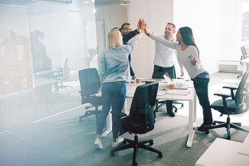 Smiling coworkers standing around an office table high fiving to