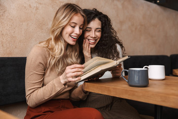 Wall Mural - Pretty girls friends sitting in cafe drinking coffee reading book.