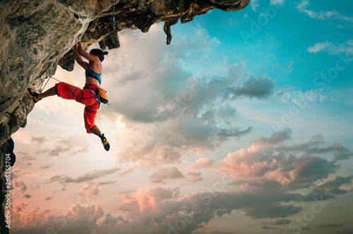 Fotomural Athletic Woman climbing on overhanging cliff rock with sunrise sky background