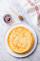 Wall Mural - Crepes, blini, thin pancakes with honey on a white plate. Marble background. Top view.