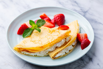 Wall Mural - Crepes, thin pancakes with cream cheese, ricotta and fresh strawberries. Marble background.