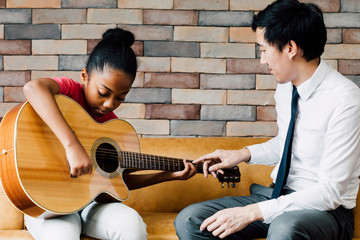 young asian male teacher giving a guitar lesson and teaching how to play guitar to african american 