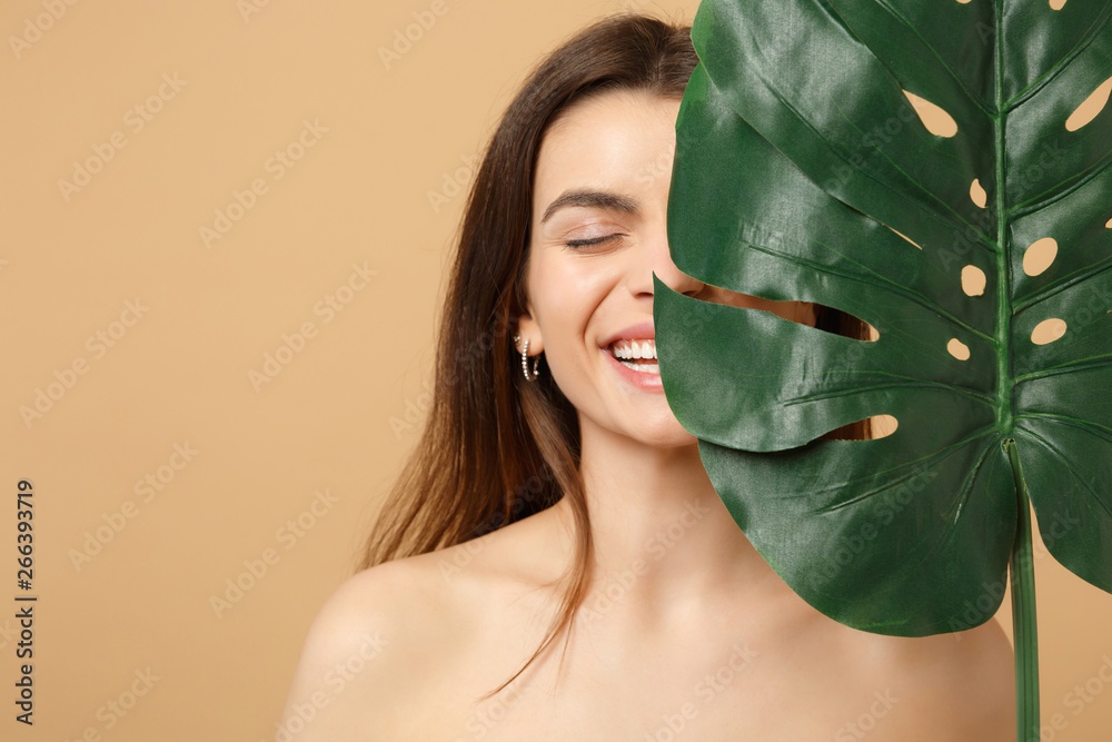 Close up brunette half naked woman 20s with perfect skin, nude make up palm leaf isolated on beige pastel wall background, studio portrait. Health care cosmetic procedures concept. Mock up copy space. - obrazy, fototapety, plakaty 