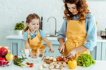 Wall Mural - cute daughter helping mother cooking vegetables at kitchen