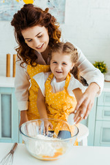 Wall Mural - happy mother with excited daughter standing together near bowl with eggs and flour in kitchen