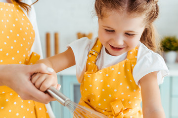 Wall Mural - mother holding excited daughter in yellow polka dot apron with balloon whisk