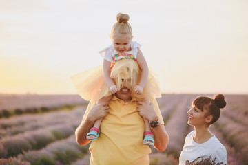 Young family in yellow clothes walk on purple lavender flower meadow field background, have fun, play with little cute child baby girl. Mother father, small kid daughter. Outdoors summer day concept.