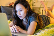 © MEM Studio/Stocksy - Young woman browsing on her laptop at a bed in a  bedroom
