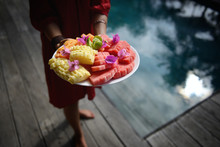 Woman In A Sundress Holding A Platter Of Tropical Fruits In Front Of A Pool