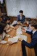 © pressahotkey - large team of people is working at one table for laptops, tablets and papers, on the background a large TV set on a wooden wall