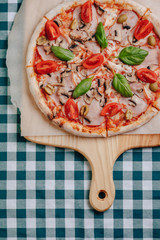 Neapolitan pizza with mushrooms, cheese, arugula, basil, tomatoes sprinkled with cheese on a wooden board on a tablecloth in a cell with a place for the text