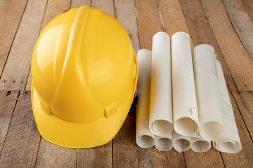 Construction helmet and roll of parchment with design. Construction engineer accessories on a wooden table.