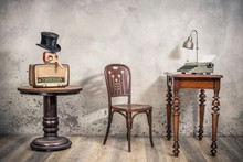 Vintage Loft Room With Antique Chair, Broadcast Radio, Carnival Mask, Cylinder Hat, Old Typewriter And Lamp On Oak Wooden Desk Front Concrete Wall Background With Shadows. Retro Style Filtered Photo