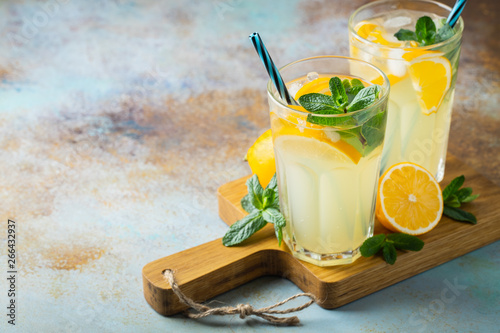 Fotografía Two glass with lemonade or mojito cocktail with lemon and mint, cold refreshing drink or beverage with ice on rustic blue background