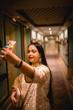© PranayChandra - waist up picture of a girl wearing traditional wear, ear ring, necklace standing in a vintage corridor of with lamps, decor and carpet floor.Taking a picture of self.