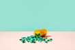 © Matthew Roharik - Colorful Prescription Pills Spilling Out of RX Medicine Bottle on Pale Pink Surface  with blue green background.