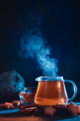 Wall Mural - Glass teapot with rising steam and star-shaped cookies on a dark background with copy space. Astronomy themed