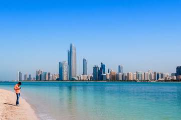Tourists on beach at marina island with modern Abu Dhabi skyline cityscape