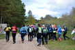 Group of athletes running forward rural road, participants of orienteering or rogaining sport competition wearing sportswear and backpacks run in cold spring day, back view.