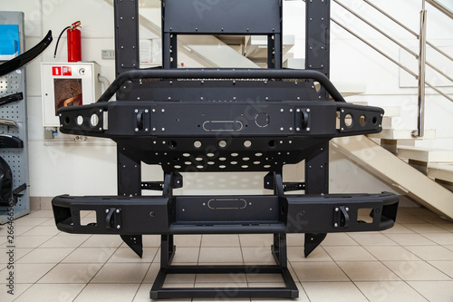 Stand for demonstration of car body elements reinforced for off-road and made of metal, such as bumper, steps and black grille in the workshop for the installation and tuning of SUV vehicles.