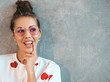 Closeup portrait of young beautiful smiling woman looking at camera. Trendy girl in casual summer white dress and sunglasses. Funny and positive female posing near gray wall in studio. Thinking