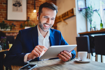 Wall Mural - Businessman sitting in cafe looking at tablet during phone call through wireless headphones