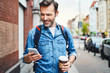 © baranq - Man using phone with wireless headphones walking in the city and drinking coffee