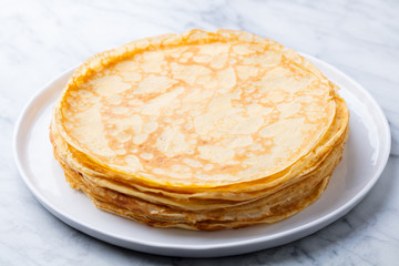 Wall Mural - Crepes, thin pancakes with honey on a white plate. Marble background. Close up.