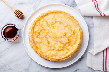 Wall Mural - Crepes, thin pancakes with honey on a white plate. Marble background. Top view.