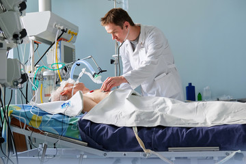 Intensive care caucasian doctor examines intubated critical stance patient writing notes to case report in intensive care department