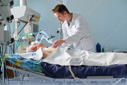 Intensive care caucasian doctor examines intubated critical stance patient writing notes to case report in intensive care department