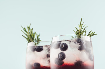 Elegant summer fresh drinks with ice cubes, blueberry, rosemary on fashion pastel mint color background, closeup, top section, details.