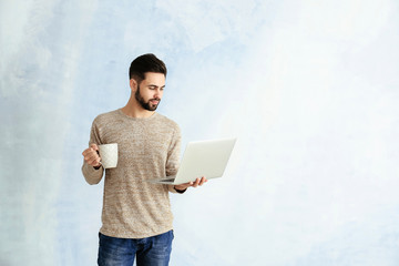 Poster - Male programmer with laptop and cup of coffee on color background