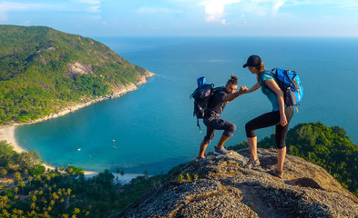 man and woman hiking on the top of cliff in summer mountains at morning time and enjoying view of na