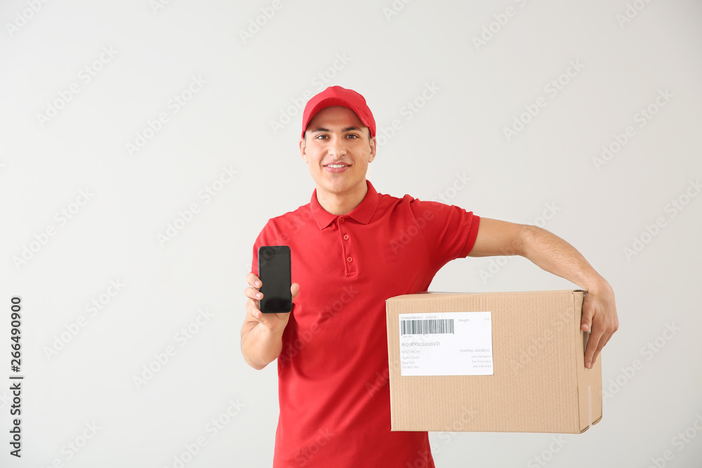 Delivery man with box and mobile phone on light background