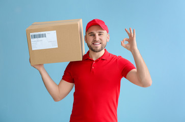 Handsome delivery man with box showing OK on color background