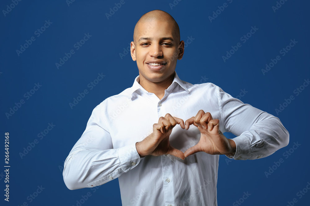 Handsome African-American man making heart with his hands on color background